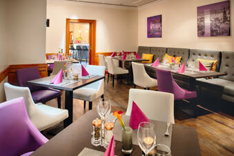 Dining area at Leonardo Hotel Heidelberg with purple and white chairs, tables set with pink napkins and glassware
