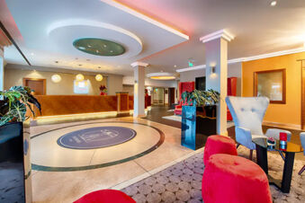 Spacious lobby area in Leonardo Hotel Heidelberg with a reception desk, red and gray chairs, plants, and modern ceiling lights
