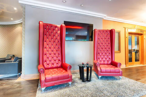Two tall red leather tufted armchairs with a small black table between them in Leonardo Hotel Heidelberg lobby