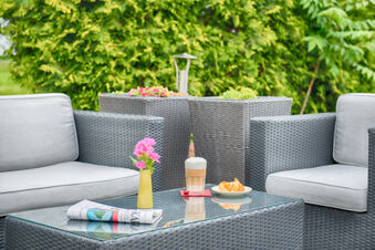 Outdoor seating area with grey wicker furniture, glass table holding flowers, coffee, croissants, and a newspaper at Leonardo Hotel Heidelberg