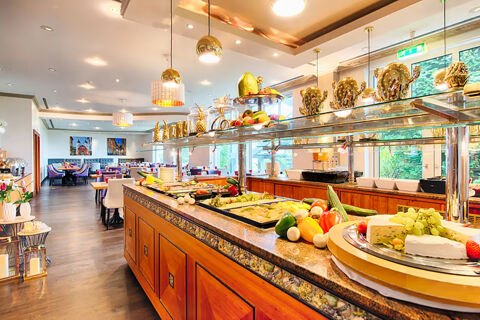 Buffet area with various fresh vegetables, cheeses, and fruit displayed on a counter inside Leonardo Hotel Heidelberg dining room