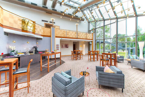 Spacious lobby area at Leonardo Hotel Heidelberg with large windows, wooden tables, gray armchairs, and buffet setup along the wall