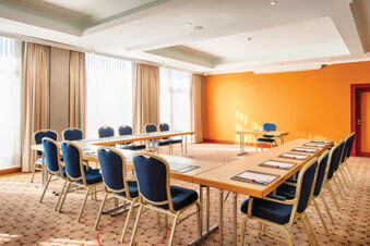 Meeting room at Leonardo Hotel Heidelberg with U-shaped tables, blue chairs, notepads, pens, and large windows with curtains