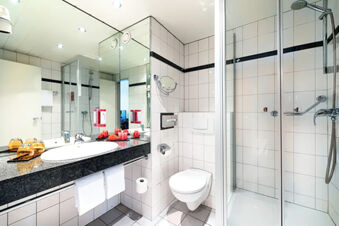 Modern bathroom at Leonardo Hotel Heidelberg with white tiles, wall-mounted toilet, glass shower and black granite countertop