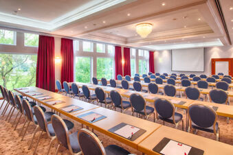 Conference room with rows of blue chairs and tables with notepads and pens at Leonardo Hotel Heidelberg