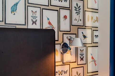 A close-up of a wall with framed bird, butterfly, and leaf illustrations above a dark brown headboard with a lit wall lamp at Gasthaus Backmulde - Hotel