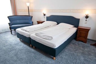 Kamar hotel sederhana dengan dua tempat tidur single, sofa biru dan meja samping tempat tidur kayu di Gasthaus Backmulde - Hotel.