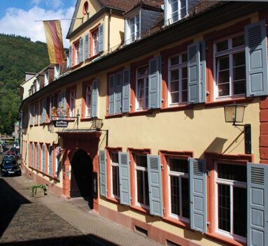 Fassade des historischen Gasthaus Backmulde - Hotel mit pastellgelben W&auml;nden, blauen Fensterl&auml;den und rotem Fachwerk unter blauem Himmel.