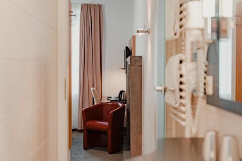 View of a hotel room with a red armchair, desk, kettle, cup, television, and window with pink curtains at Gasthaus Backmulde - Hotel