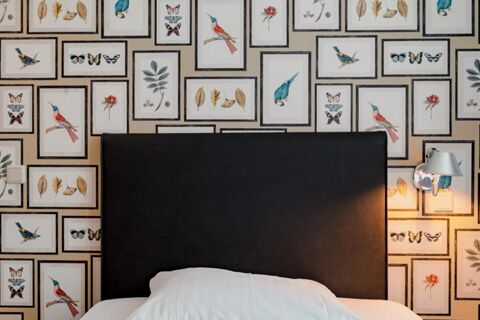 Black headboard with white bedding beneath wall covered in framed bird, butterfly, flower, and leaf illustrations at Gasthaus Backmulde - Hotel