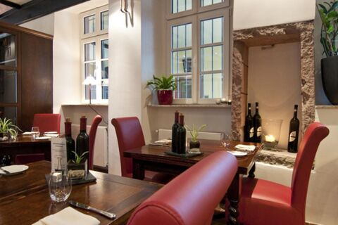 Dining area at Gasthaus Backmulde - Hotel with wooden tables, red chairs, wine bottles, plants, and stone wall accents