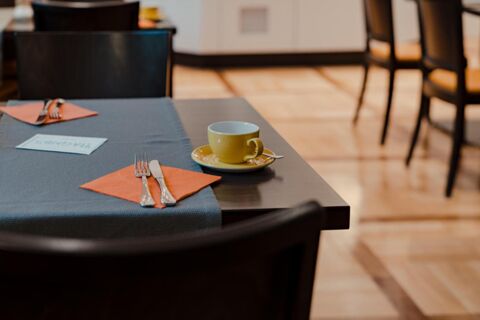 Table set with a yellow cup and saucer, silverware on orange napkins, and a menu card at Gasthaus Backmulde - Hotel