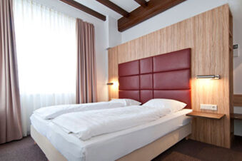 Kamar hotel modern dengan dua tempat tidur single, kepala tempat tidur berlapis kain merah dan panel kayu di Backmulde Inn - Hotel.