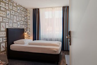 Single bed with white linens next to a window with sheer and striped curtains in Gasthaus Backmulde - Hotel room