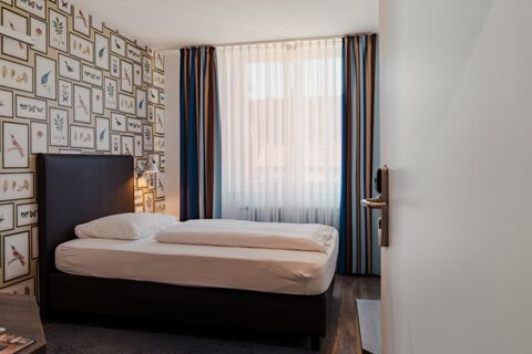 Single bed with white linens next to a window with sheer and striped curtains in Gasthaus Backmulde - Hotel room