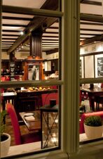 View through a window into a dining area with red chairs, wooden beams, framed pictures, and a decorative cabinet at Gasthaus Backmulde - Hotel