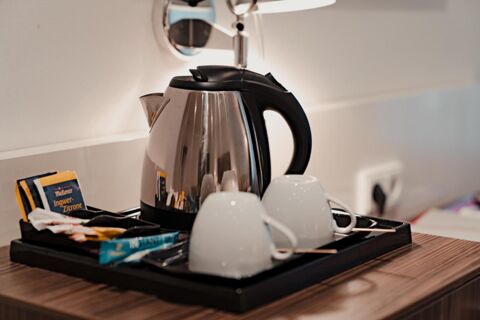 Electric kettle with black handle, white cups with saucers, and assorted tea bags on a tray at Gasthaus Backmulde - Hotel