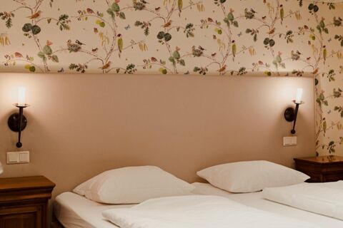 Double bed with two white pillows, floral wallpaper with birds, and two lit wall lamps in Gasthaus Backmulde - Hotel