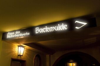 Illuminated signboard reading Haus des B&auml;ckerhandwerks Backmulde with a symbol above an entrance at Gasthaus Backmulde - Hotel