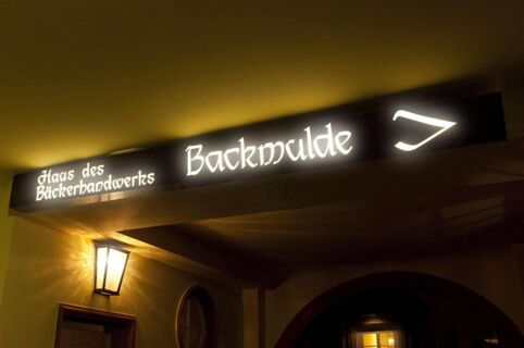 Illuminated signboard reading Haus des B&auml;ckerhandwerks Backmulde with a symbol above an entrance at Gasthaus Backmulde - Hotel