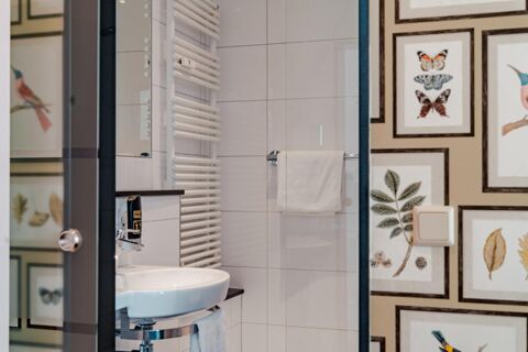 Bathroom with white sink, towel hanging on a rack, a radiator, and butterfly and bird framed prints at Gasthaus Backmulde - Hotel