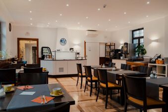 Dining area with black chairs and tables set with yellow cups and orange napkins at Gasthaus Backmulde - Hotel