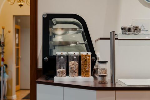 Three transparent cereal dispensers with different cereals on a counter next to a black bread slicer at Gasthaus Backmulde - Hotel