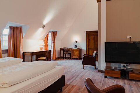 Spacious hotel room at Gasthaus Backmulde - Hotel with two beds, wooden desks, orange curtains, TV, and leather chairs.