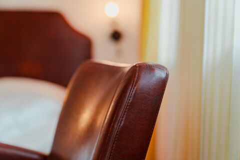 Close-up of the brown leather headboard and armrest in a room at Gasthaus Backmulde - Hotel with light curtains and wall lamp in background