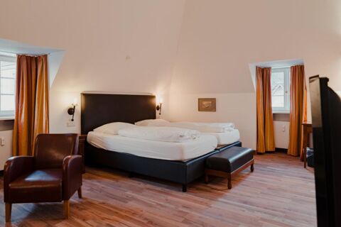 A double bed with white linens and dark headboard between two windows with orange curtains in Gasthaus Backmulde - Hotel