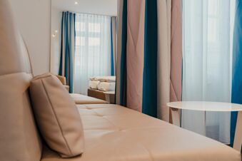 Beige cushioned sofa with pillows, white round table, and curtains with sheer and blue fabric at Gasthaus Backmulde - Hotel