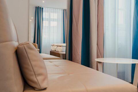 Beige cushioned sofa with pillows, white round table, and curtains with sheer and blue fabric at Gasthaus Backmulde - Hotel