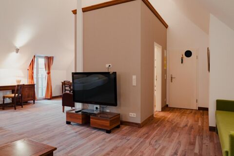 Living area of a room at Gasthaus Backmulde - Hotel with wooden floor, TV, wooden desk, chairs, orange curtains, and white walls