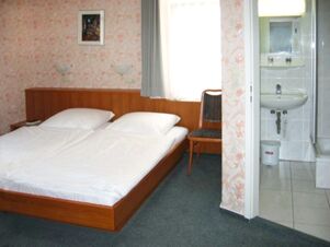 Gem&uuml;tliches Doppelzimmer mit zwei Einzelbetten und einem kleinen angrenzenden Badezimmer im Hotel Wirt am Berg mit floralem Tapetendesign.