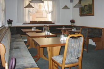 Gem&uuml;tlicher Gastraum mit Holztischen und gepolsterten Sitzb&auml;nken im Hotel Wirt am Berg, dekoriert mit Pflanzen und Bildern.