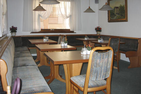 Gem&uuml;tlicher Gastraum mit Holztischen und gepolsterten Sitzb&auml;nken im Hotel Wirt am Berg, dekoriert mit Pflanzen und Bildern.