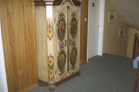 Flur mit einem kunstvoll bemalten Holzschrank und Zimmert&uuml;r Nummer 21 im Hotel Wirt am Berg mit Teppichboden und Holzverkleidung.