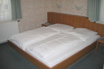 Schlicht eingerichtet Doppelzimmer im Hotel Wirt am Berg mit zwei getrennten Betten, Holzrahmen und floralem Tapetendesign.