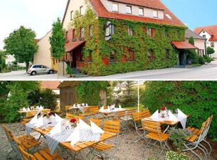 Building covered with green ivy and red roof labeled Gasthof zur Sonne with outdoor seating area of wooden tables and chairs