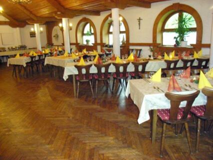 Interior view of Gasthof zur Sonne dining room with wooden chairs, tables set with yellow and orange napkins and white tablecloths
