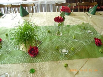 Mesa festiva no Gasthof zur Sonne com toalha de mesa verde, rosas vermelhas e acess&oacute;rios decorativos para os convidados.