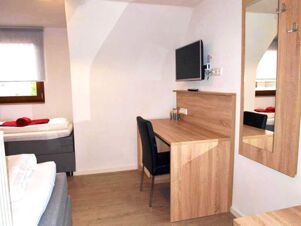 Small hotel room at Gasthof zur Sonne with a single bed, wooden desk, black chair, wall-mounted TV, and a large wall mirror