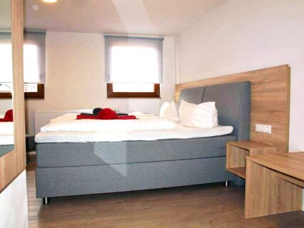 A bright hotel bedroom at Gasthof zur Sonne with a grey upholstered bed, white linens, pillows, and wooden furniture