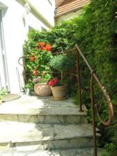 Escalier ext&eacute;rieur avec plusieurs pots de fleurs et une main courante rouill&eacute;e &agrave; l'entr&eacute;e de l'auberge "zur Sonne", entour&eacute;e d'arbustes verts.