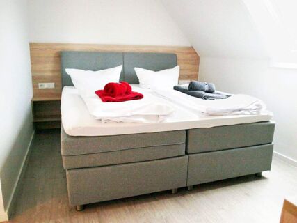 Double gray bed with white linens and red and gray towels on top in a bright room at Gasthof zur Sonne