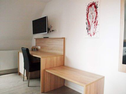 A room at Gasthof zur Sonne with a wall-mounted TV, wooden desk and bench, black chair, and abstract red and black wall art