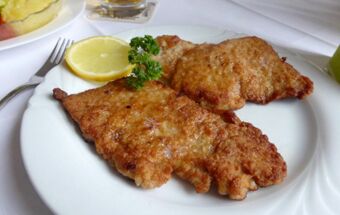 Knusprig gebratenes Wiener Schnitzel mit Zitronenscheibe und Petersilienzweig auf einem wei&szlig;en Teller im Landgasthof Schmidt serviert.