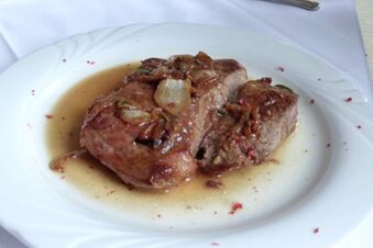 Zart gebratenes Schweinefleisch mit Zwiebeln und Sauce auf einem wei&szlig;en Teller serviert im Landgasthof Schmidt.