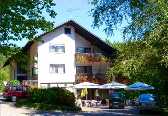 Fassade des Landgasthof-Pension Limbacher M&uuml;hle mit Balkonen, bl&uuml;henden Blumen und Schirmen vor dem Eingang bei sonnigem Wetter.