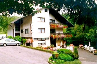 Ansicht der Landgasthof-Pension Limbacher M&uuml;hle mit blumengeschm&uuml;ckten Balkonen und Gartenbereich samt Sitzgelegenheiten im Freien.